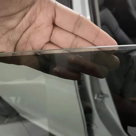 Hand at the top edge of a rolled-down window showing a clear strip of glass above the tint film