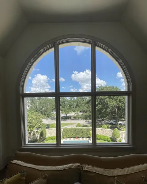 View through a tall arched window from an upstairs sitting room toward live oaks and the street