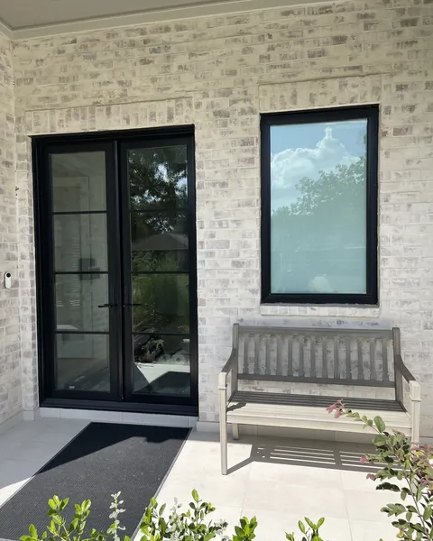 Black French doors and a window with film on a whitewashed brick porch