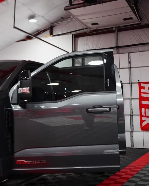 Close-up of the tinted front door glass on a gray Ford Super Duty, shop lights reflecting in the window
