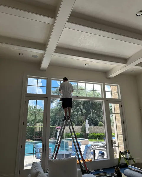 Texas Tinted installer on a ladder applying window film to the tall transom windows of a living room that overlooks a pool