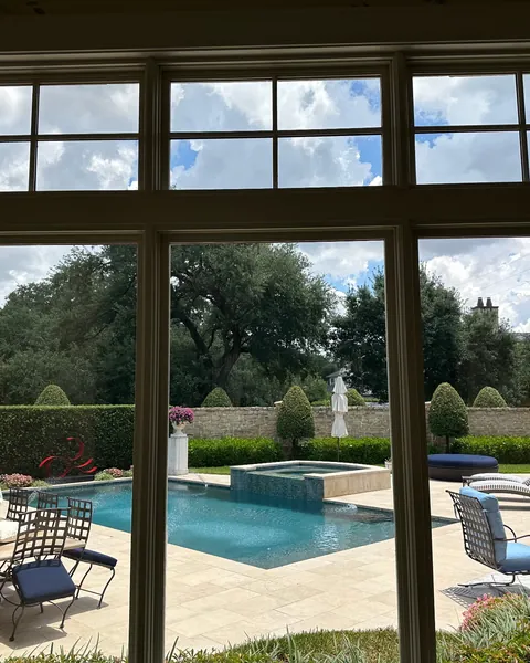 View of a backyard pool and garden through tall living room windows with clear window film