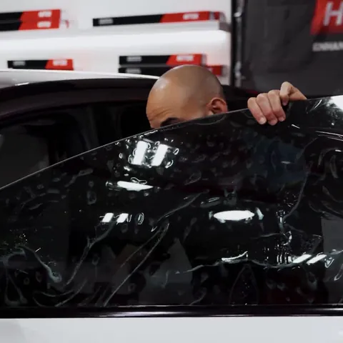 Texas Tinted installer laying a sheet of ceramic window film over the driver window of a white Lucid Gravity