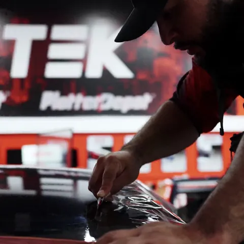Installer trimming window film on the glass roof of a Lucid Gravity, with a protective cover over the paint