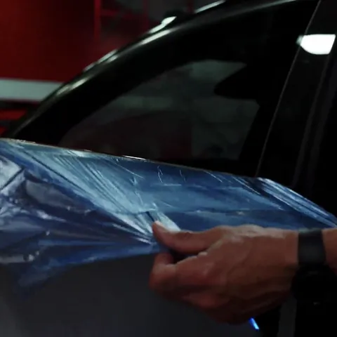 Installer pulling a blue protective shield over the door panel of a Lucid Gravity before window tinting