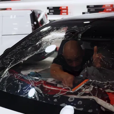 Installer inside a Lucid Gravity squeegeeing heat-rejecting film onto the windshield, with the dash covered
