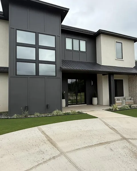 Modern two-story home with a tall grid of windows on a dark facade, the glass reflecting the sky after window film