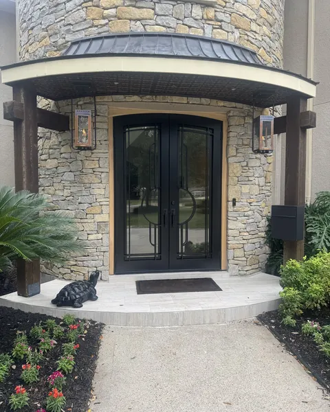 Arched black iron double doors with glass in a stone entry under copper lanterns
