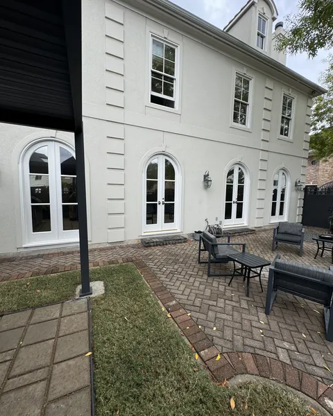 Back of a stucco home with arched French doors opening onto a brick patio